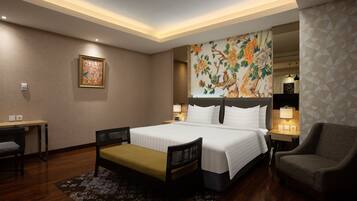 A hotel room with a large bed, a desk with a chair, a bench, a chair, and a nightstand with a lamp.