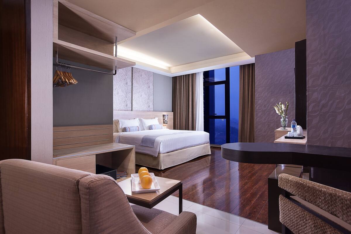 Habitación de hotel con cama, escritorio, silla, armario y vistas al exterior.