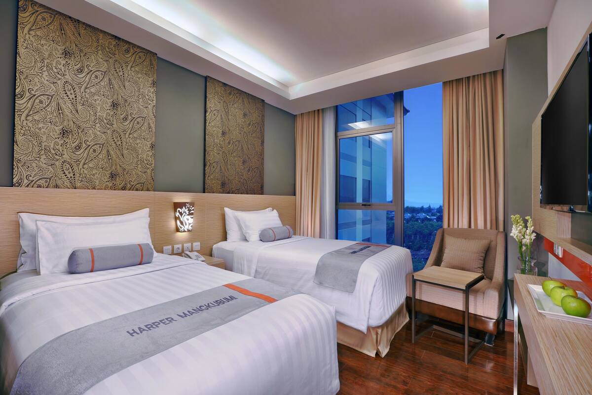 Habitación de hotel con dos camas, un escritorio, una silla y vistas a la ciudad.