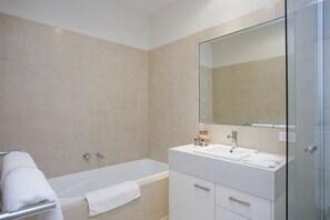 A modern bathroom with a bathtub, a glass shower enclosure, and a vanity with a mirror. - Two Bays Apartments (Torquay)