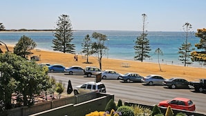 Una carretera costera con coches estacionados, una playa y árboles.