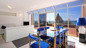 Una sala de estar moderna con una mesa de vidrio y sillas azules, un sofá blanco y un televisor.