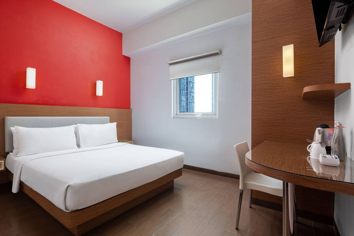 Ein modernes Hotelzimmer mit Bett, Glastisch, Sessel, Fernseher und einem Fenster mit Blick.