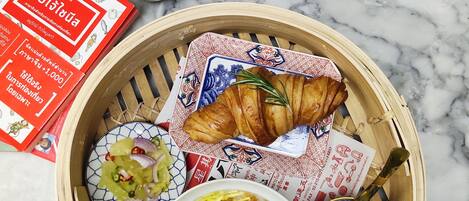 Un plato con un croissant, ensalada y sopa sobre una mesa de mármol.
