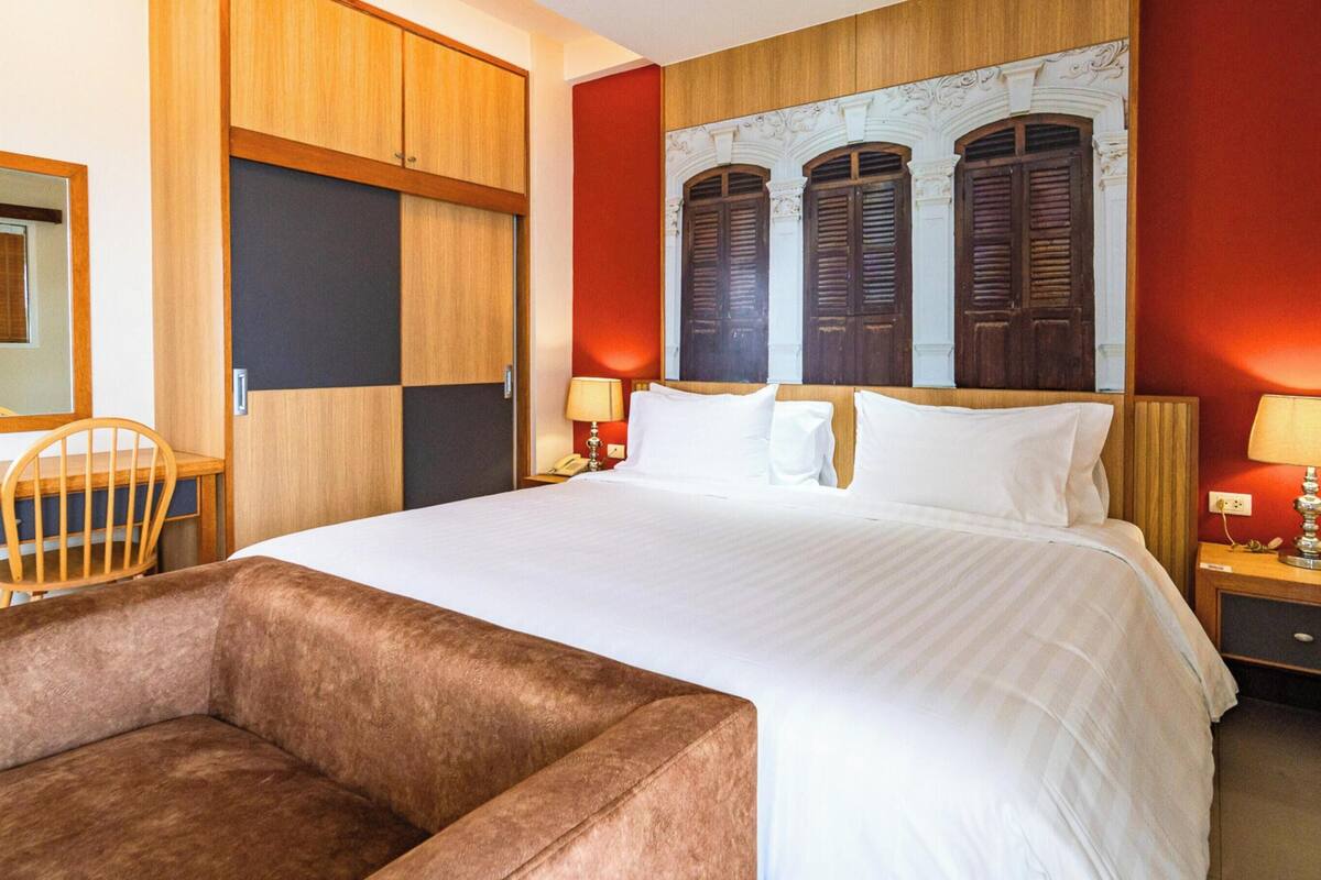 A hotel room with a large bed, a wooden wardrobe, a desk with a chair, and two bedside tables with lamps.