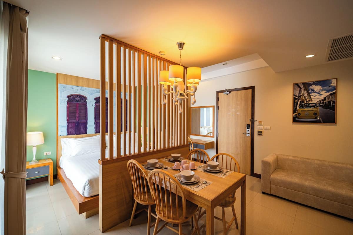 A hotel room with a bed, a dining table with chairs, a sofa, a wooden partition, and a chandelier.