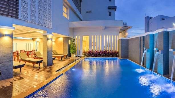A swimming pool with lounge chairs and a wooden deck, surrounded by modern buildings. - Ratana Hotel Rassada (Ratsada)
