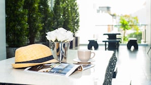 A table with a straw hat, a metal vase with white flowers, a white cup, and a magazine. - Ratana Hotel Rassada (Ratsada)