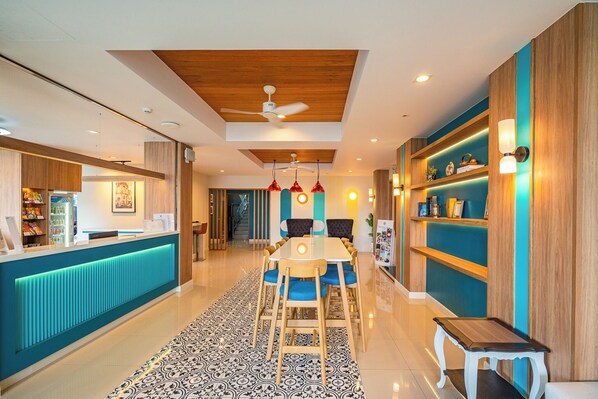 Un moderno vestíbulo de hotel con una recepción, un comedor con mesa y sillas, y una escalera que conduce a otras plantas.