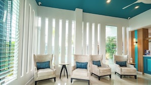 A modern hotel lobby with four armchairs, a small round table, and a view of the outdoors through large windows. - Ratana Hotel Rassada (Ratsada)
