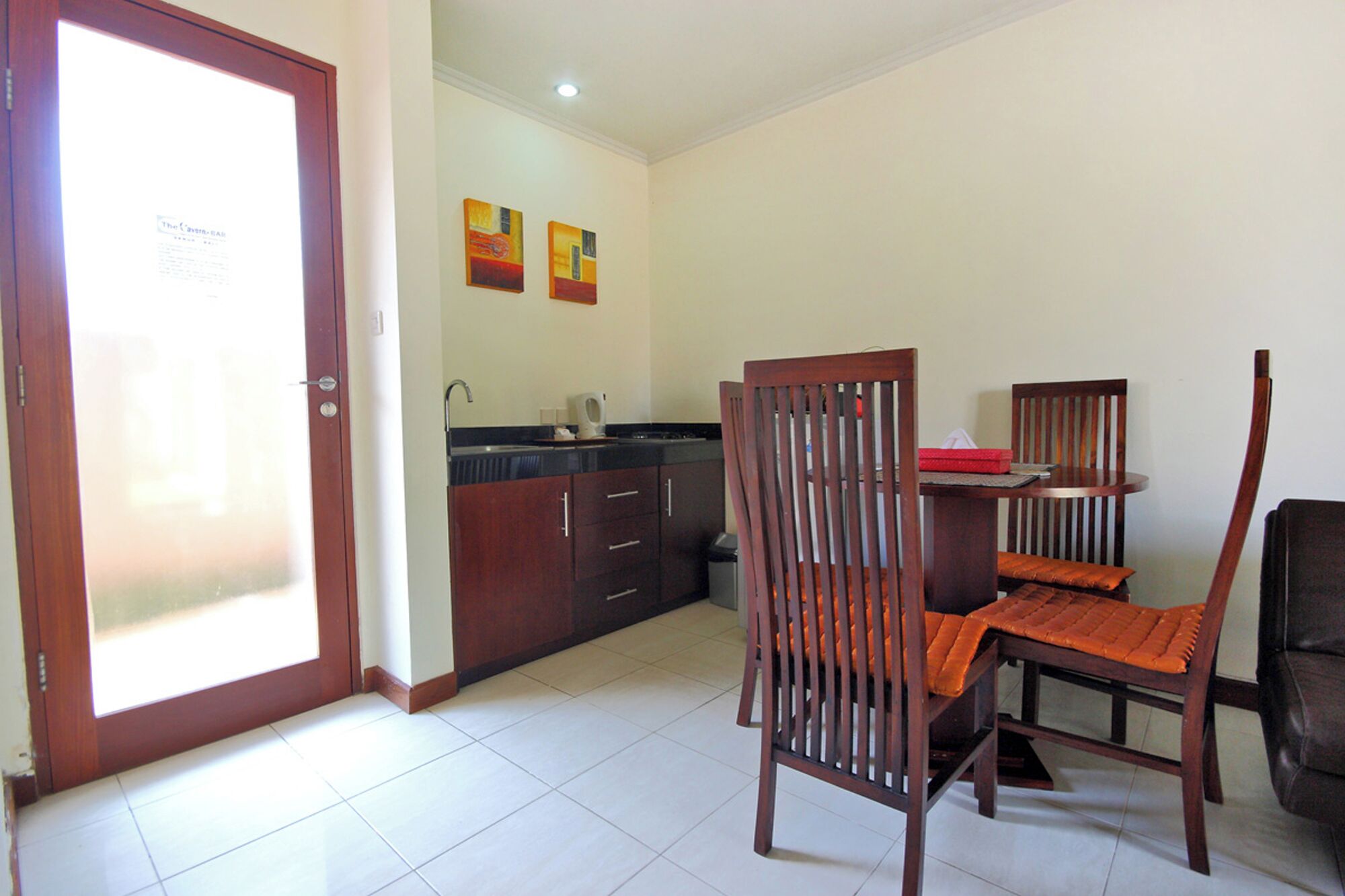 A dining area with a wooden table and chairs, a kitchen with dark cabinets, and a door with a frosted glass panel.