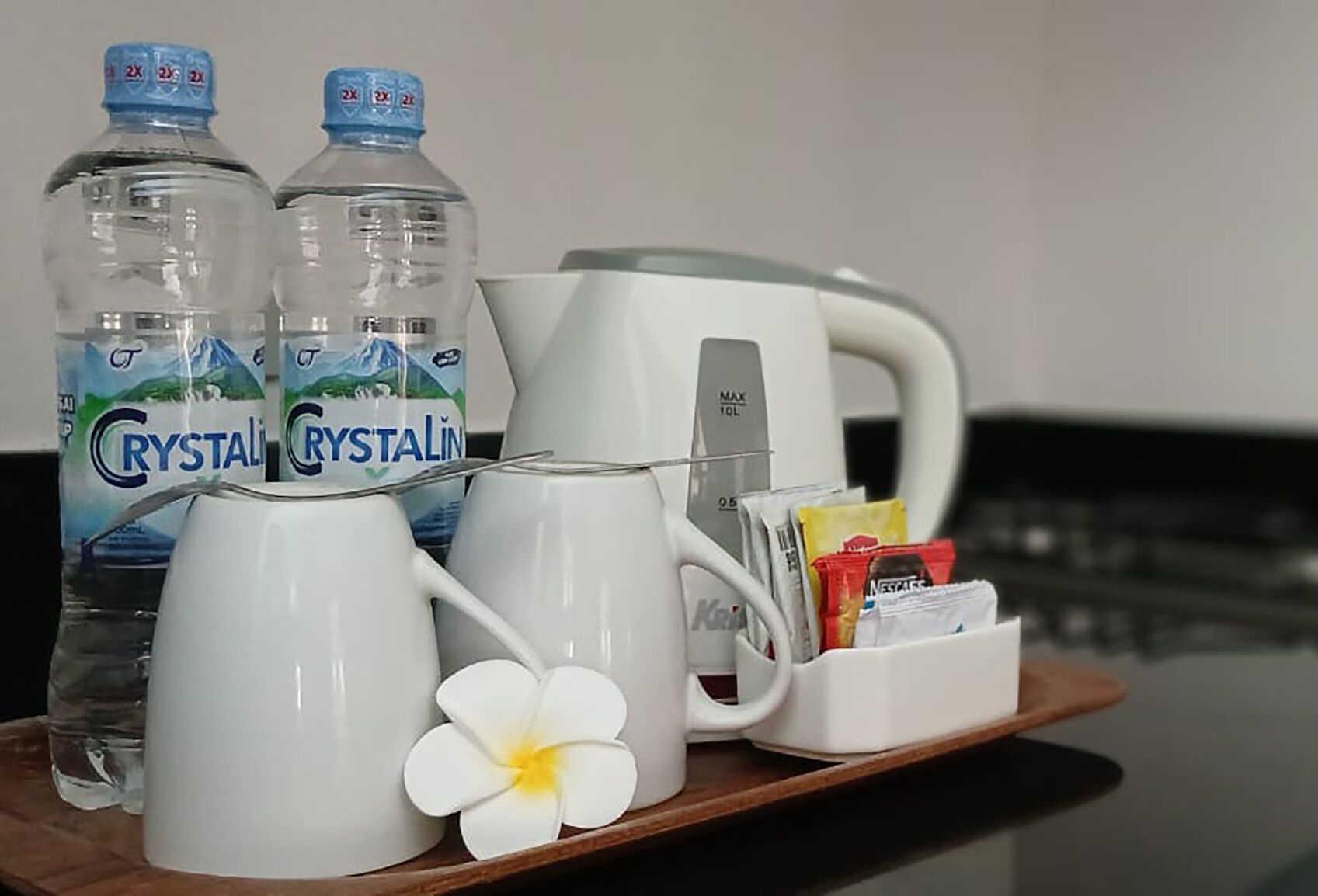 Una bandeja con dos botellas de agua Crystal Geyser, una taza blanca, una tetera blanca, una cafetera blanca y un sobre de té.