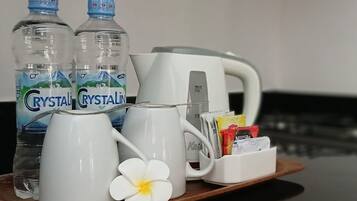 Una bandeja con dos botellas de agua Crystal Geyser, una taza blanca, una tetera blanca, una cafetera blanca y un sobre de té.