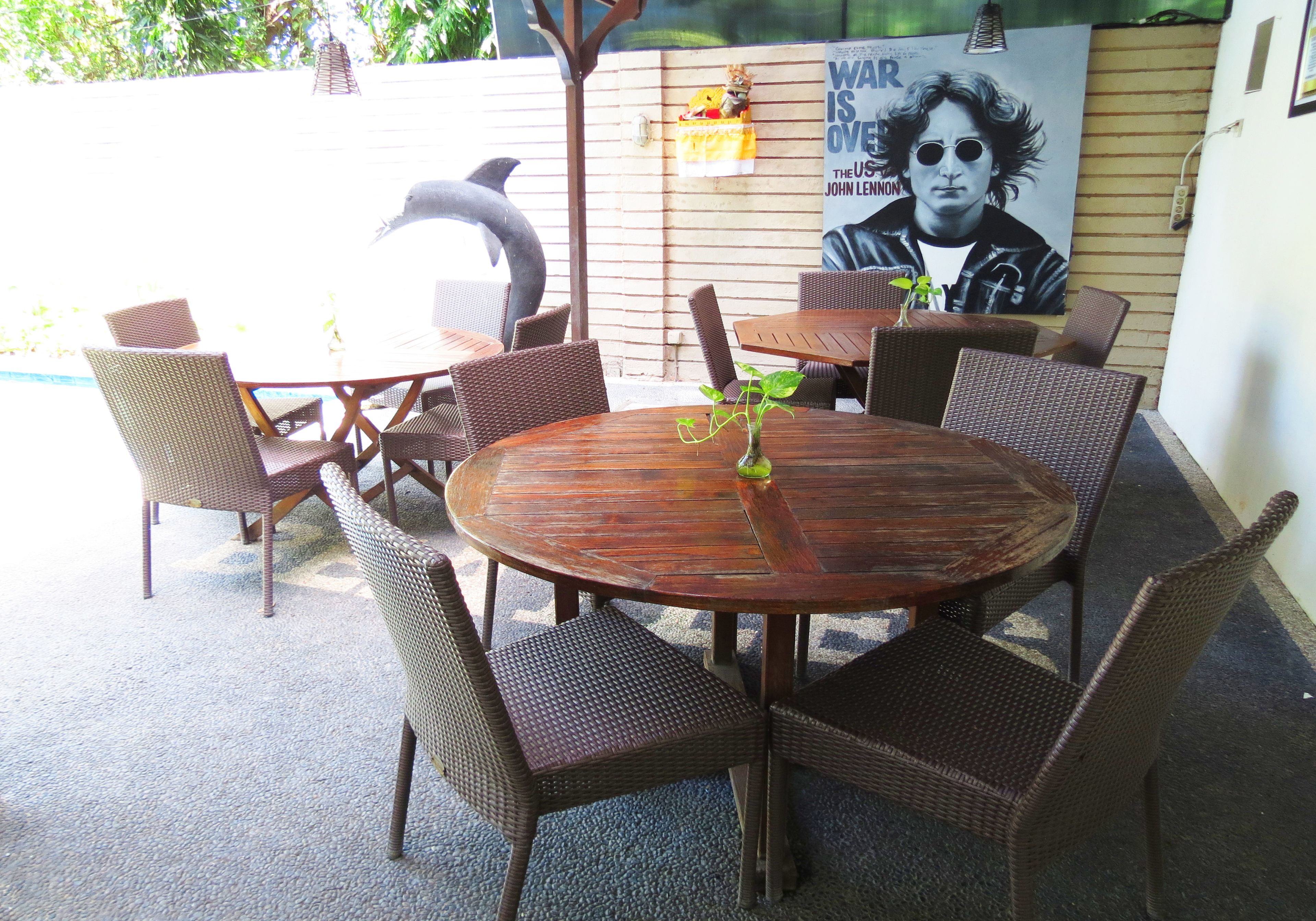 A round wooden table with wicker chairs, a potted plant, and a poster on the wall.