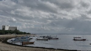 A beach with several boats docked near the shore and a building in the background. - Sekuta Condo Suites (Denpasar)