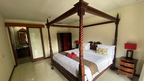 A four-poster bed with a wooden frame, a bedside table with drawers, a red lamp, and a mirror above the bed. - Sekuta Condo Suites (Denpasar)