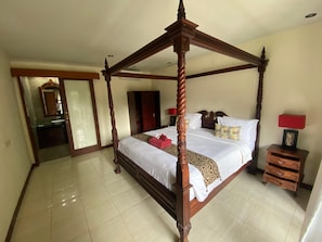 A four-poster bed with a wooden frame, a bedside table with drawers, a red lamp, and a mirror above the bed. - Sekuta Condo Suites (Denpasar)