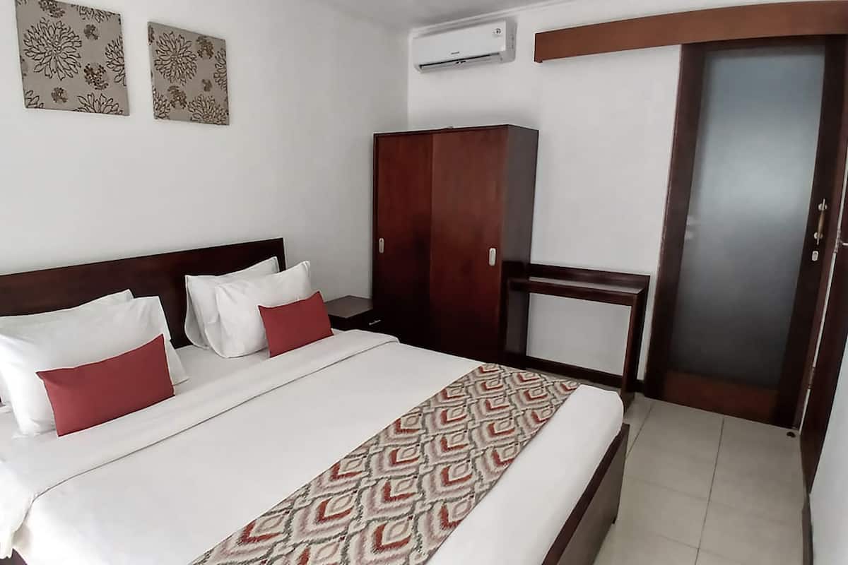 A hotel room with a bed, a wardrobe, a nightstand, and a wall-mounted air conditioner.