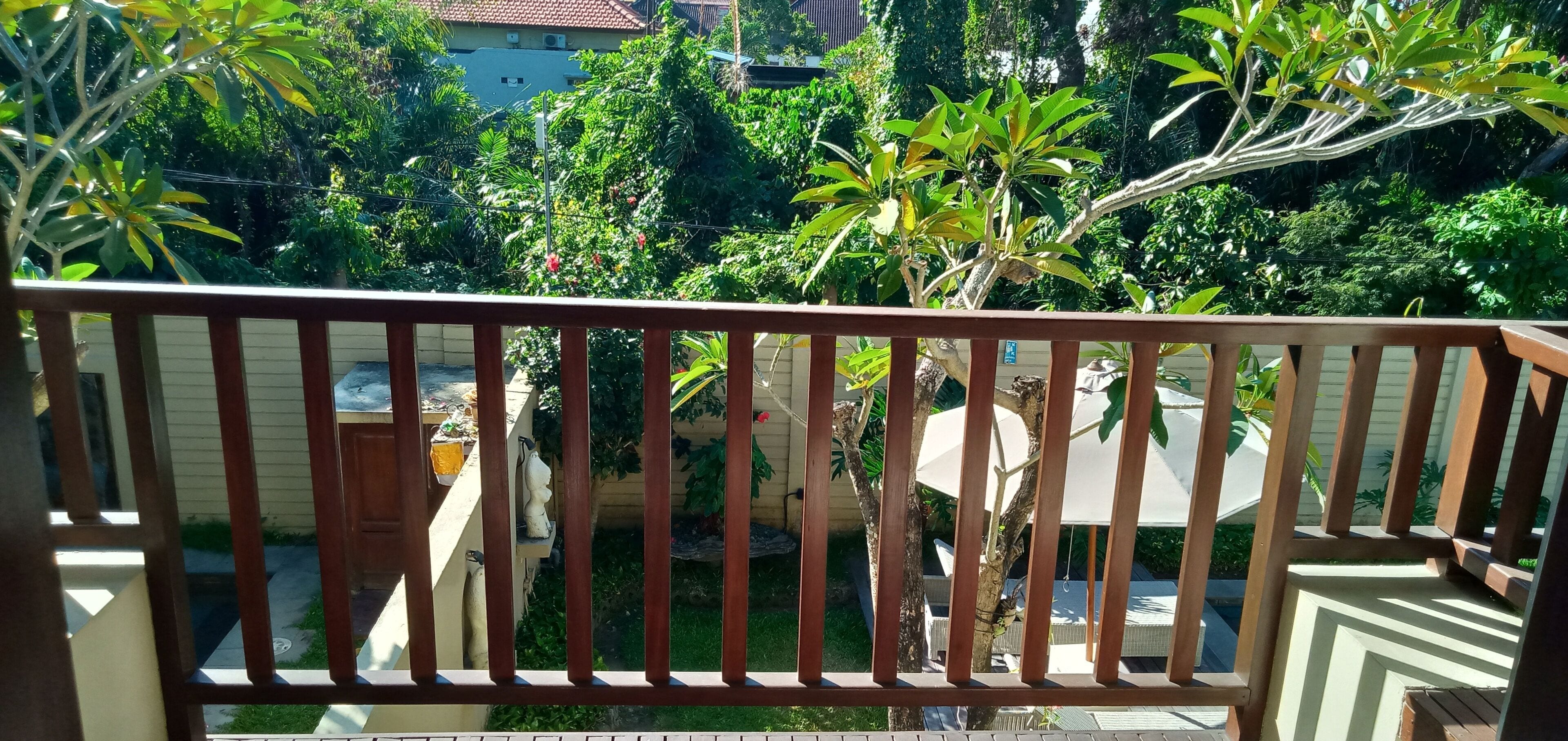 A balcony with a wooden railing, a small garden area with various plants, and a view of neighboring buildings.
