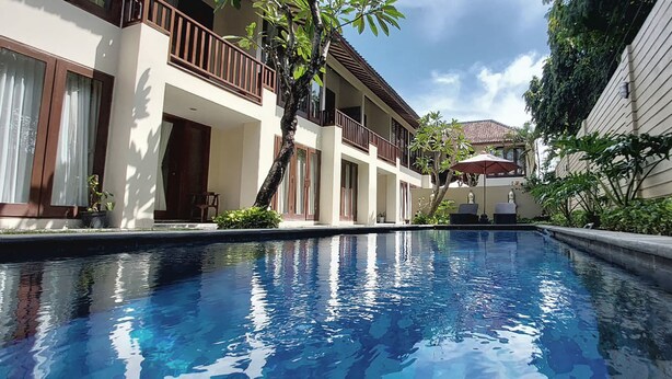 A swimming pool with a clear blue water surface, surrounded by a building with balconies and potted plants. - Sekuta Condo Suites (Denpasar)