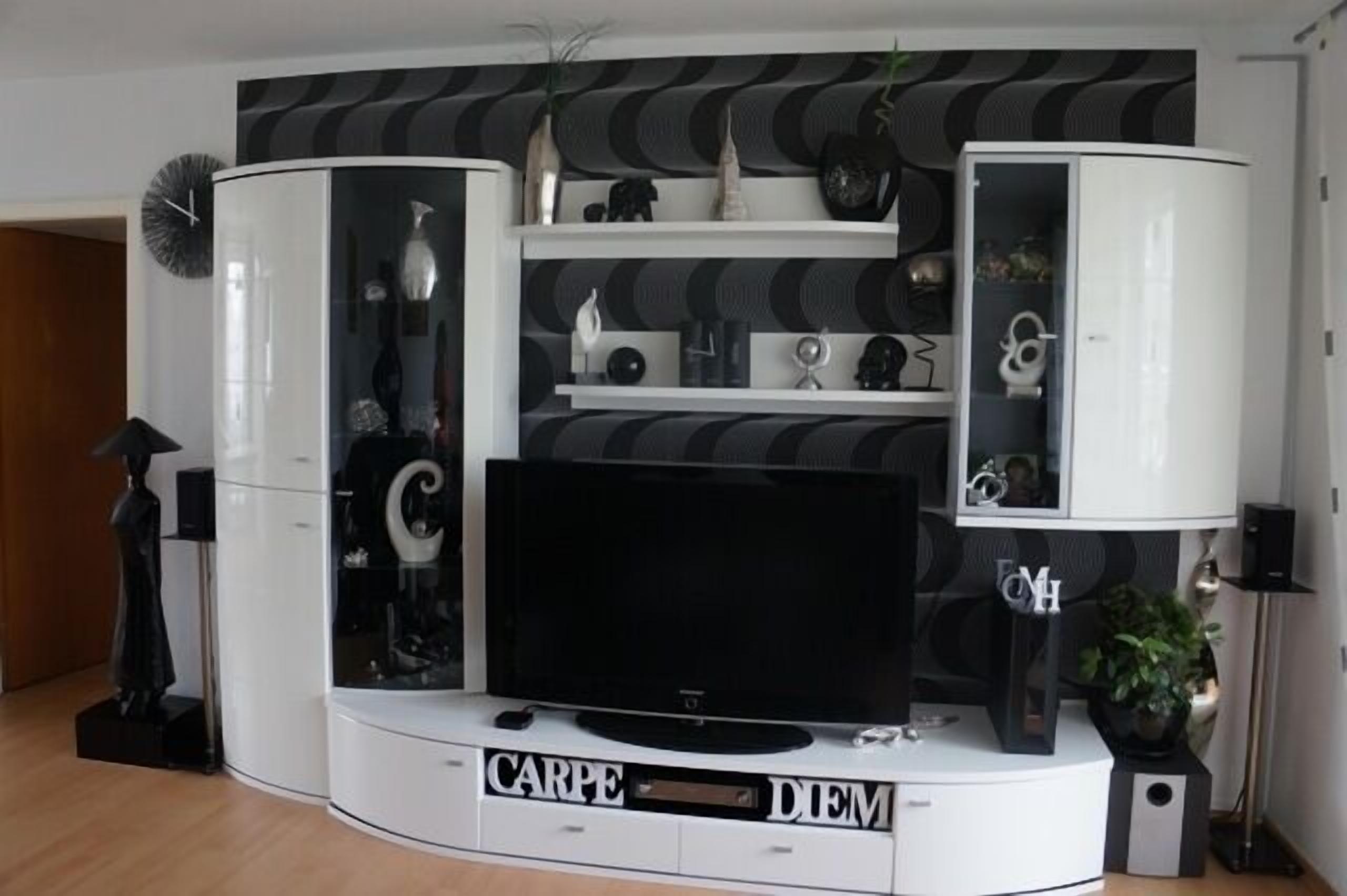Een moderne woonkamer met een flatscreen televisie, witte kasten en decoratieve items.