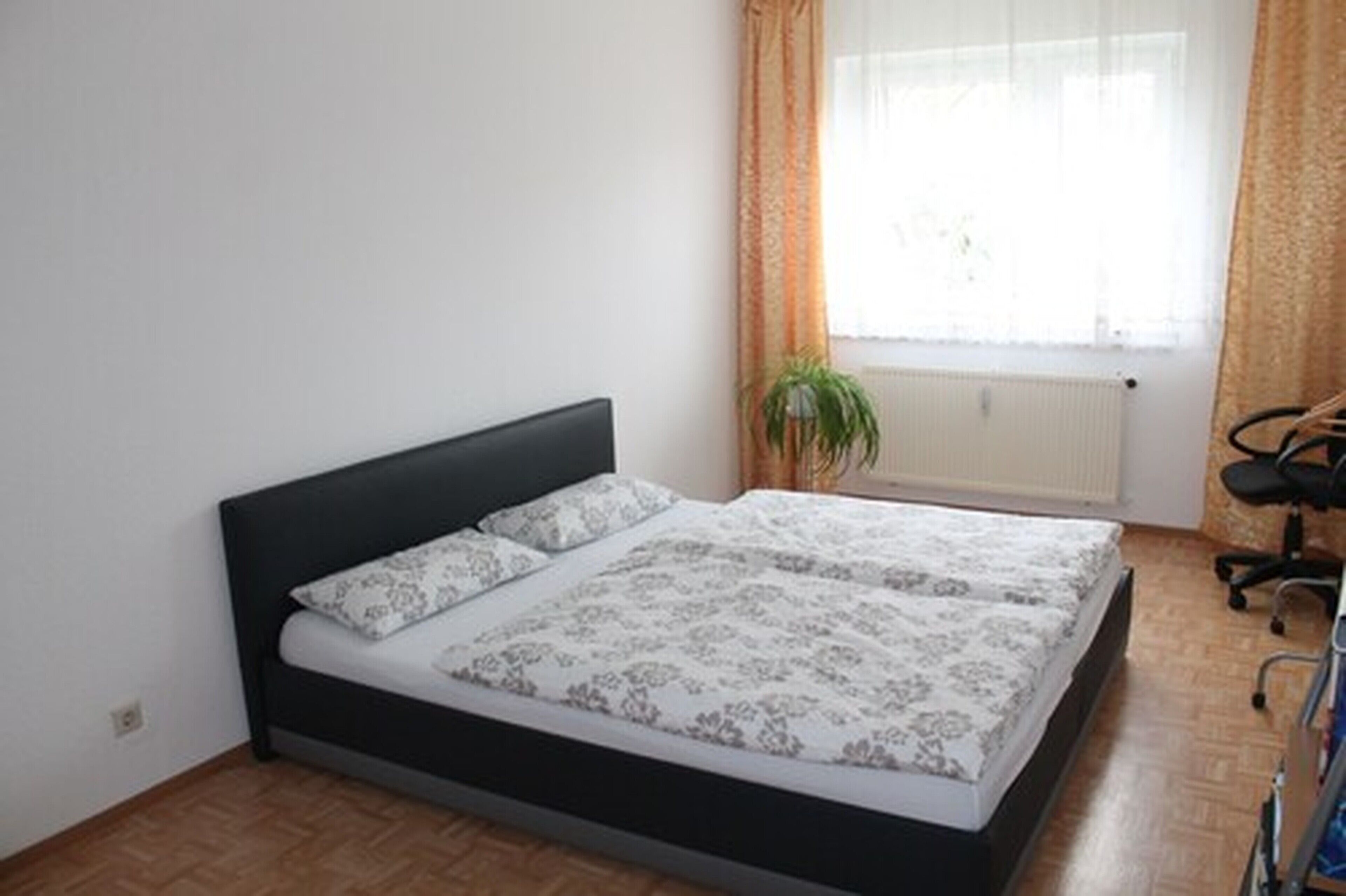 Quarto com cama, radiador, planta em vaso e uma cadeira.
