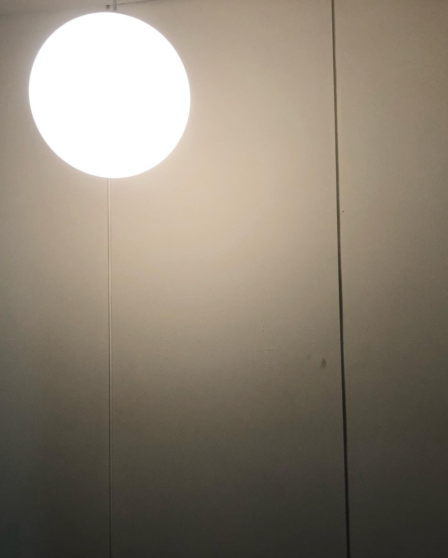 Eine schlichte Wand mit einer einzelnen, runden, weißen Leuchte, die von der Decke hängt.