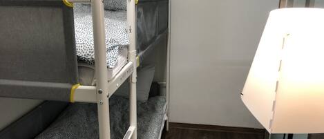 A bunk bed room with a ladder, a bedside table, and a lamp.