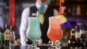 Two cocktails with straws and garnishes on a bar counter.