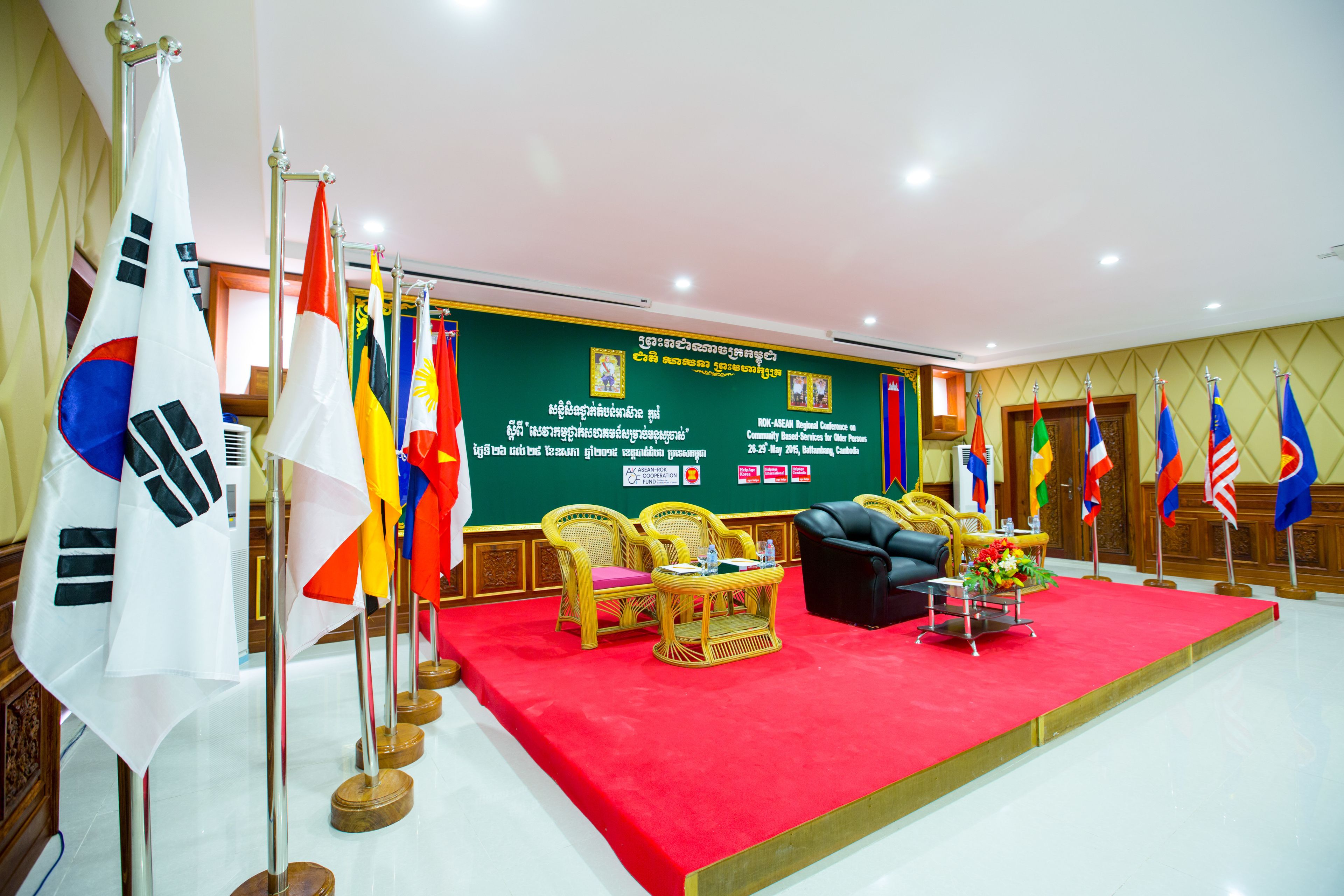 A formal meeting room with multiple flags, a red carpet, and wicker chairs.
