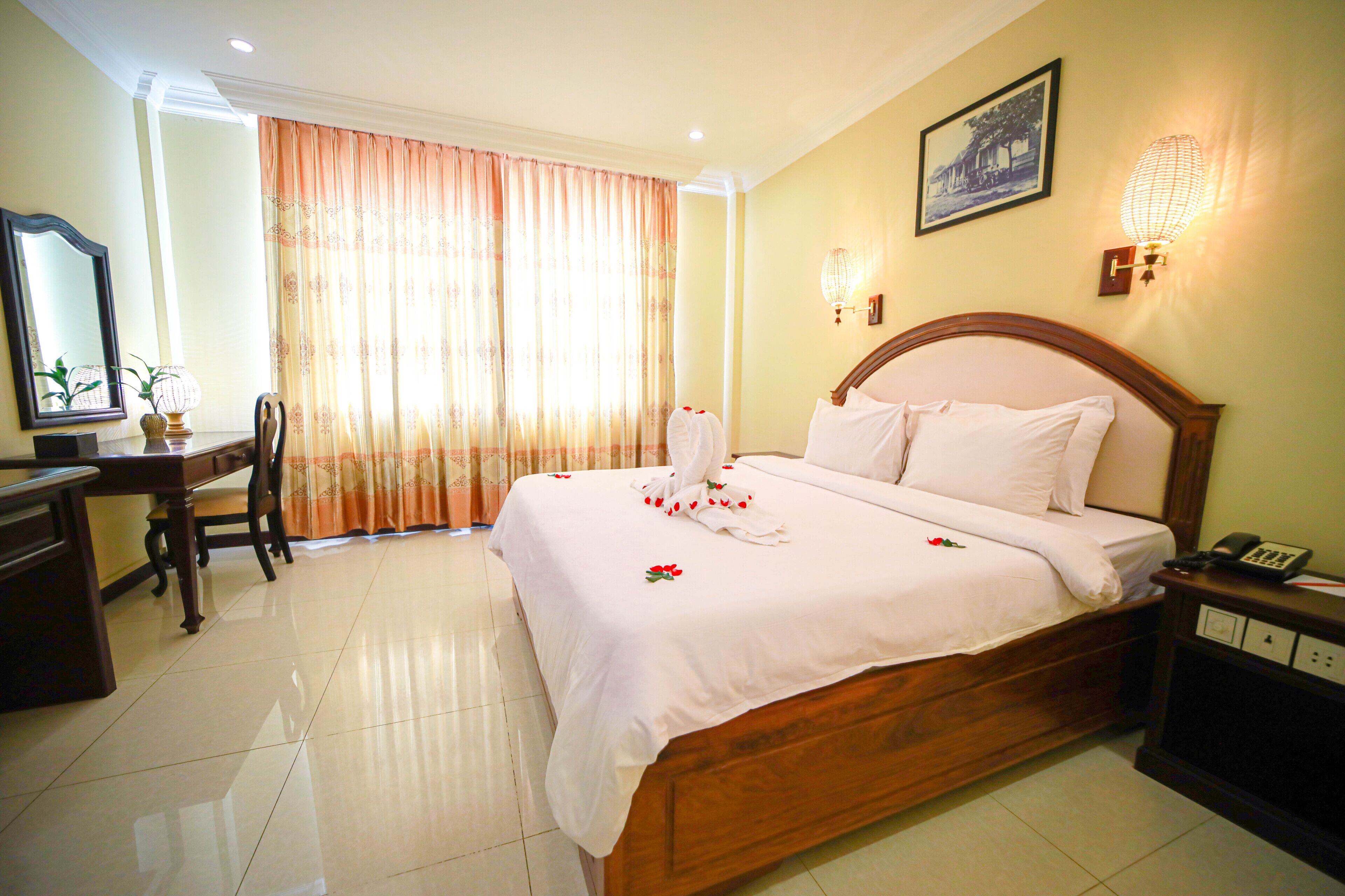 Quarto de hotel bem arrumado, com uma cama grande, uma mesa de trabalho e uma cadeira.