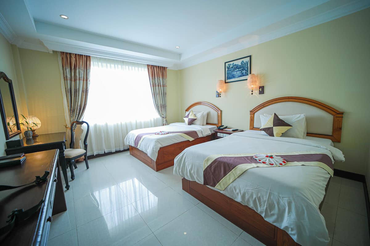 A hotel room with two beds, a desk, a chair, and a large window with curtains.