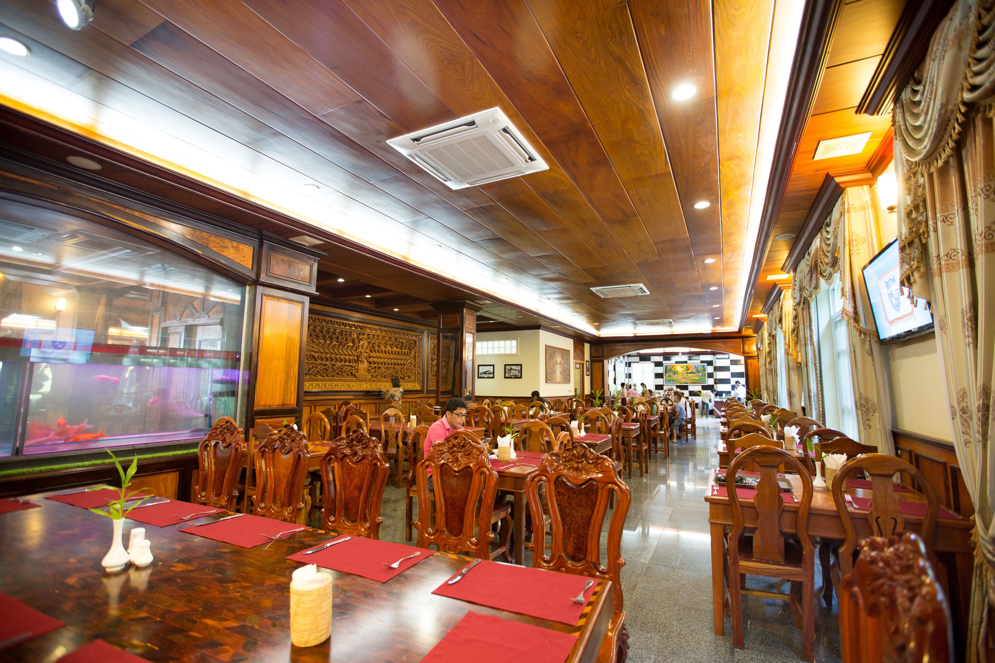 Un restaurante con mesas y sillas de madera, manteles individuales rojos y un acuario al fondo.