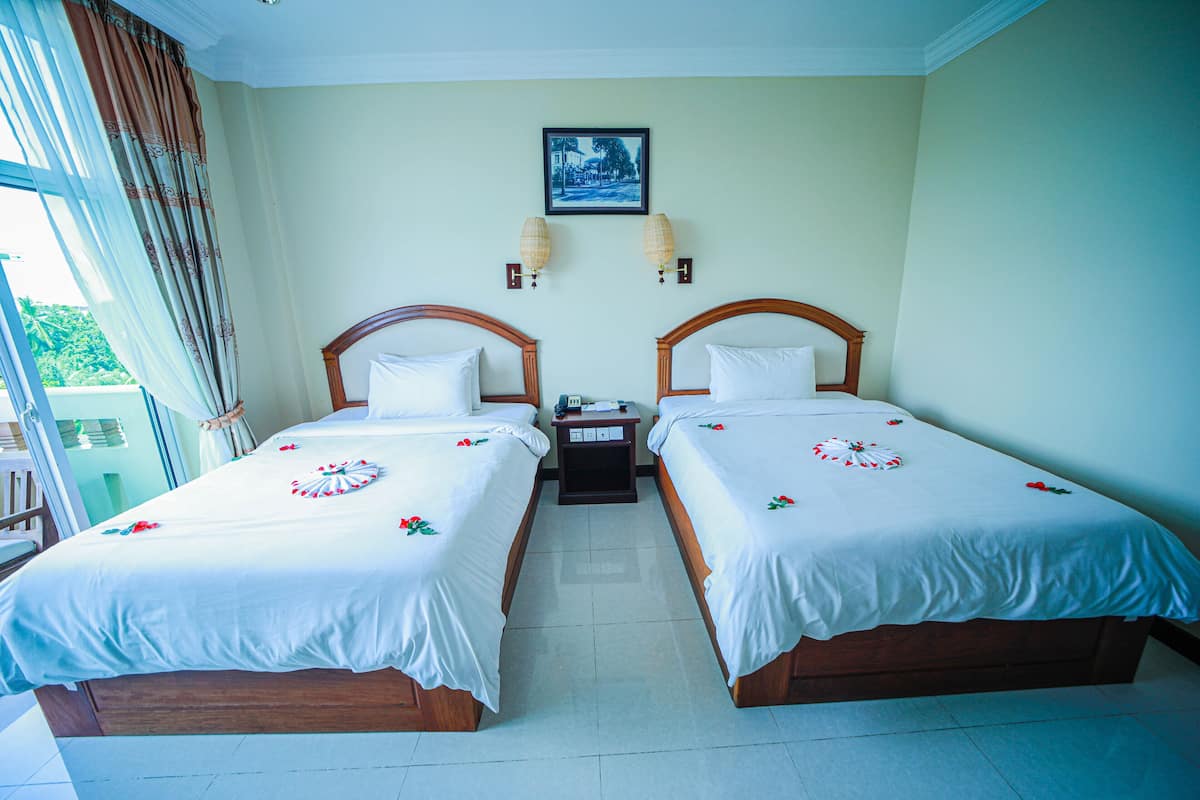 A hotel room with two single beds, a nightstand, a framed picture on the wall, and a window with curtains.