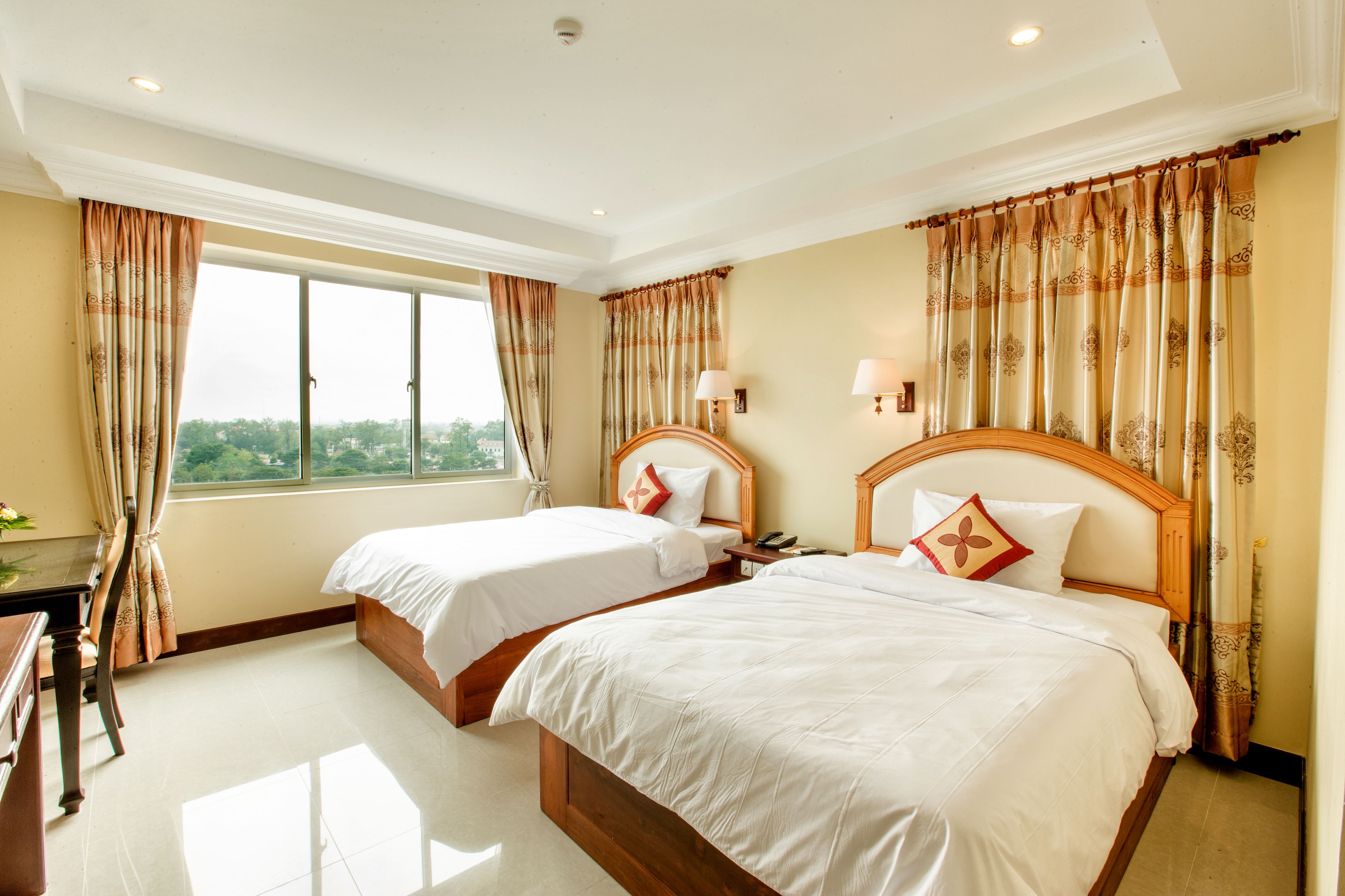 A hotel room with two beds, a desk, and a window with curtains.