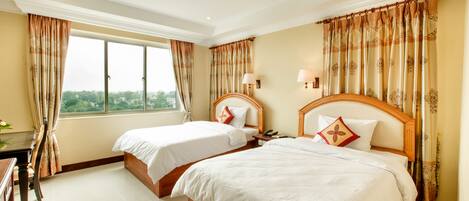 A hotel room with two beds, a desk, and a window with curtains.