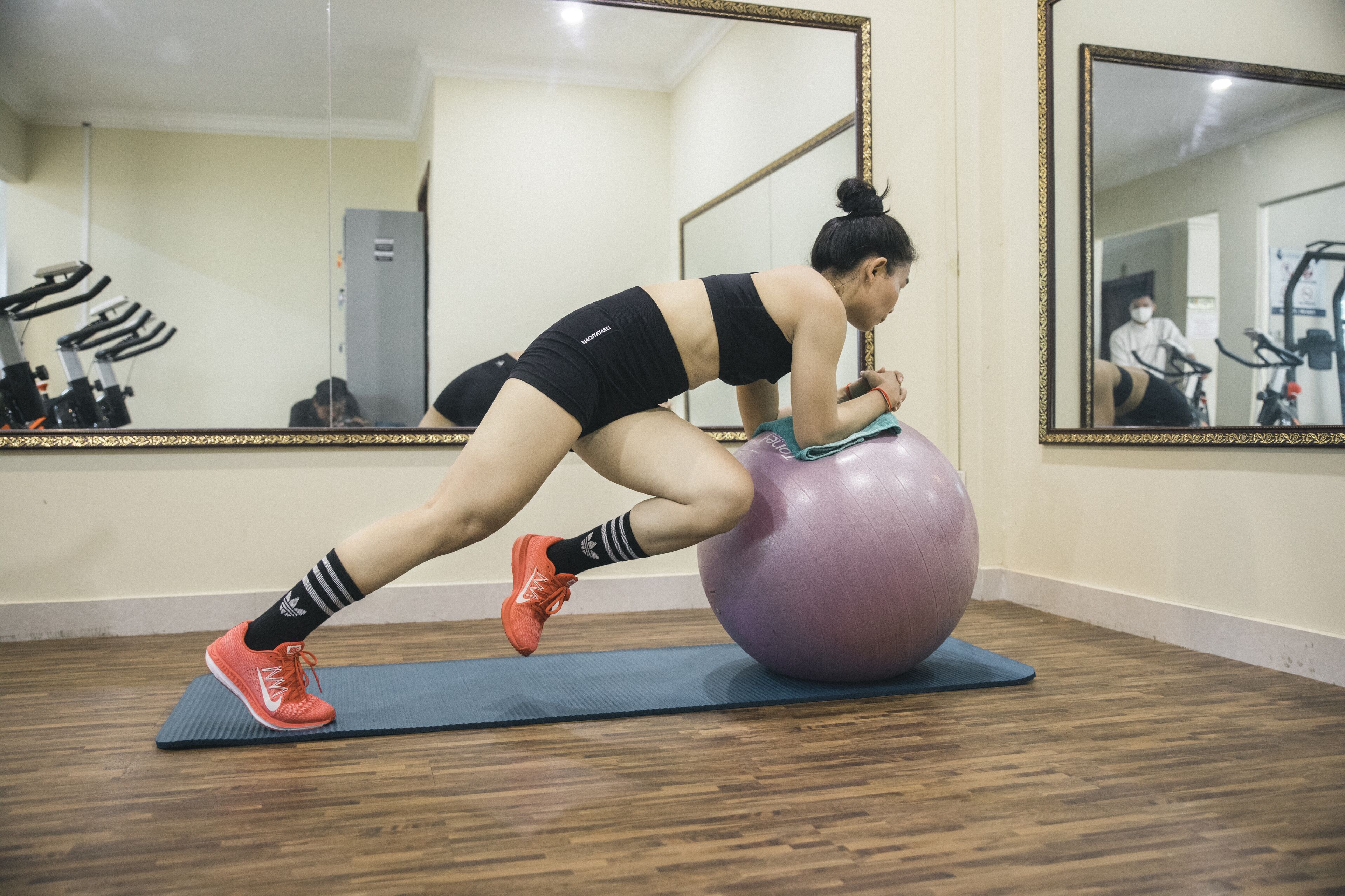 A person performing a workout on an exercise ball in a room with a mirror and exercise equipment.
