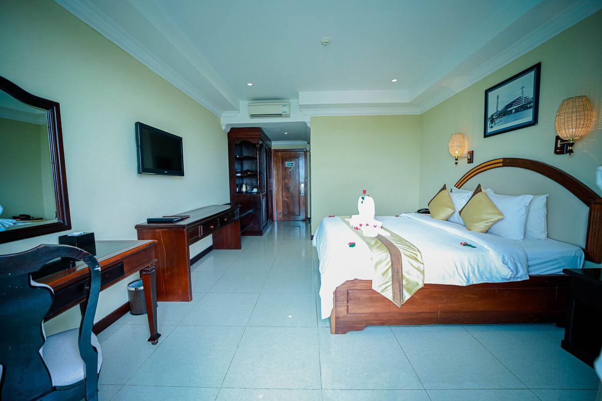 A hotel room with a bed, desk, chair, TV, and a hallway leading to another room.