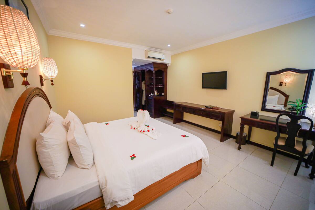 A hotel room with a bed, bedside table, desk, chair, TV, and wardrobe.