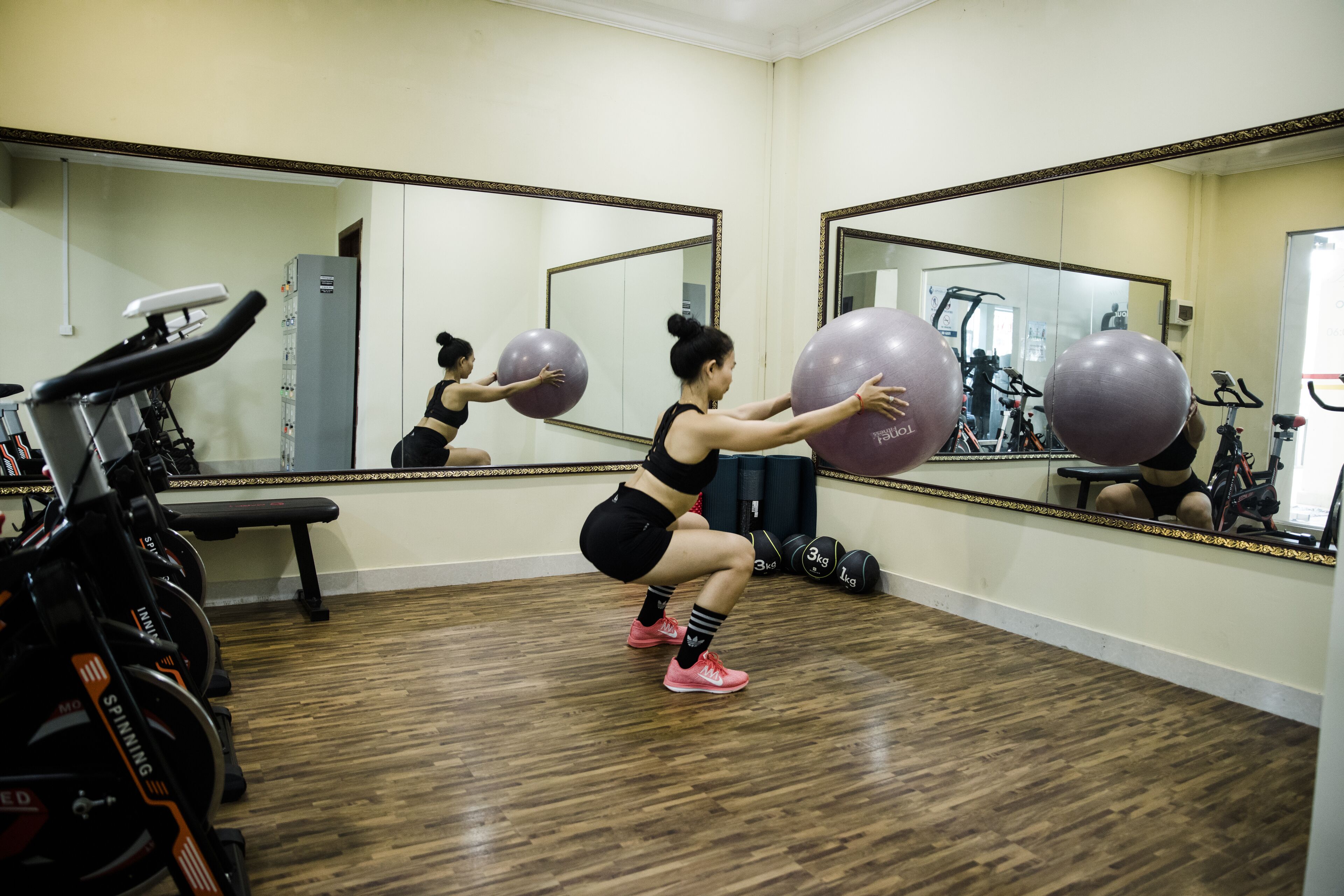A gym with exercise equipment, a large mirror, and a wooden floor.