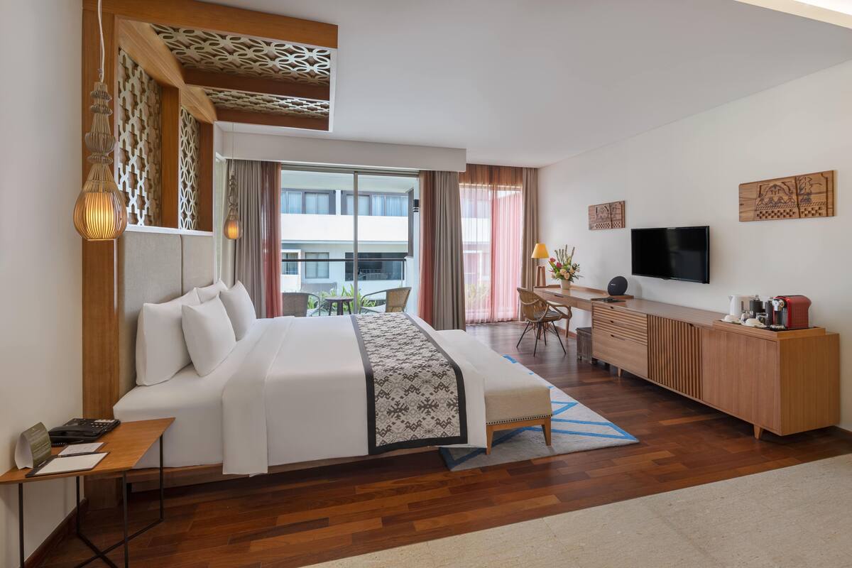 Habitación de hotel con cama, escritorio, televisor y vistas al exterior.