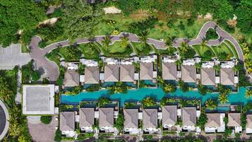 An aerial view of a resort with a central swimming pool, multiple bungalow-style accommodations, and a roundabout.