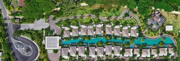 Eine Vogelperspektive zeigt ein Resort mit einem zentralen Schwimmbecken, mehreren bungalowsähnlichen Unterkünften und einer Kreisverkehr.