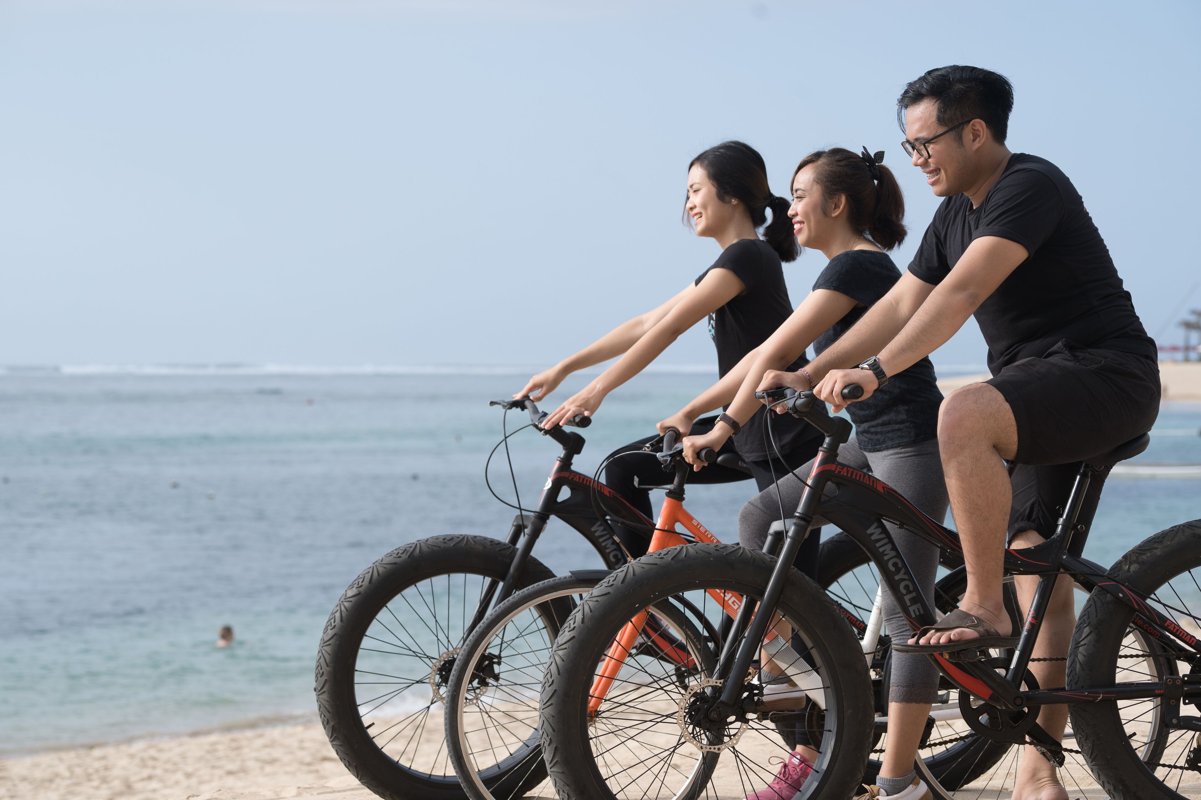 Three people on bicycles near a beach with the ocean in the background.
