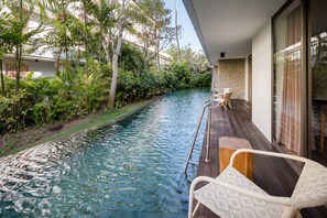 Une piscine dotée d’une terrasse en bois, entourée d’une végétation luxuriante et d’un mur de pierre.