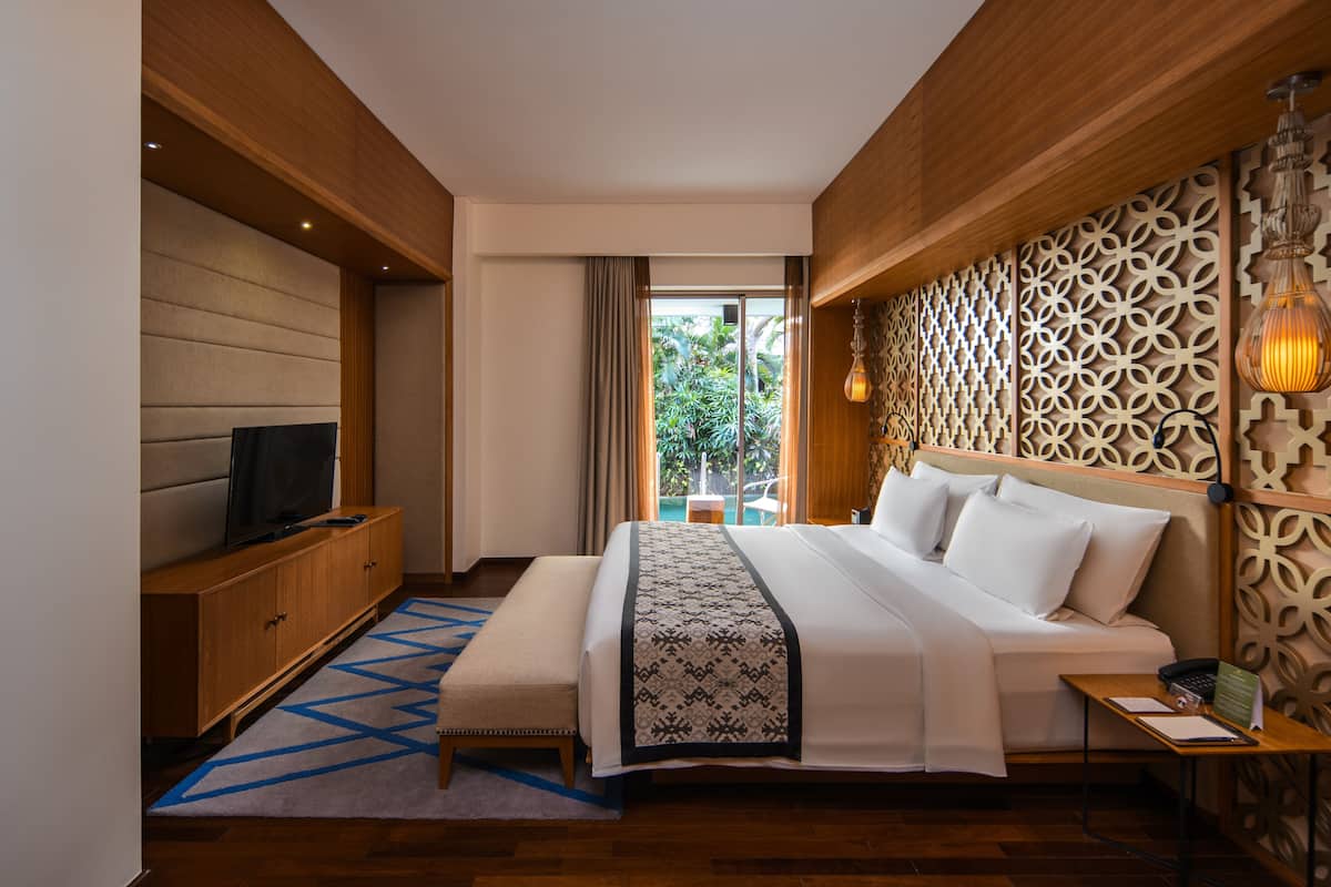Una habitación de hotel moderna con una cama grande, un televisor sobre un mueble de madera, una alfombra estampada y un panel decorativo en la pared.