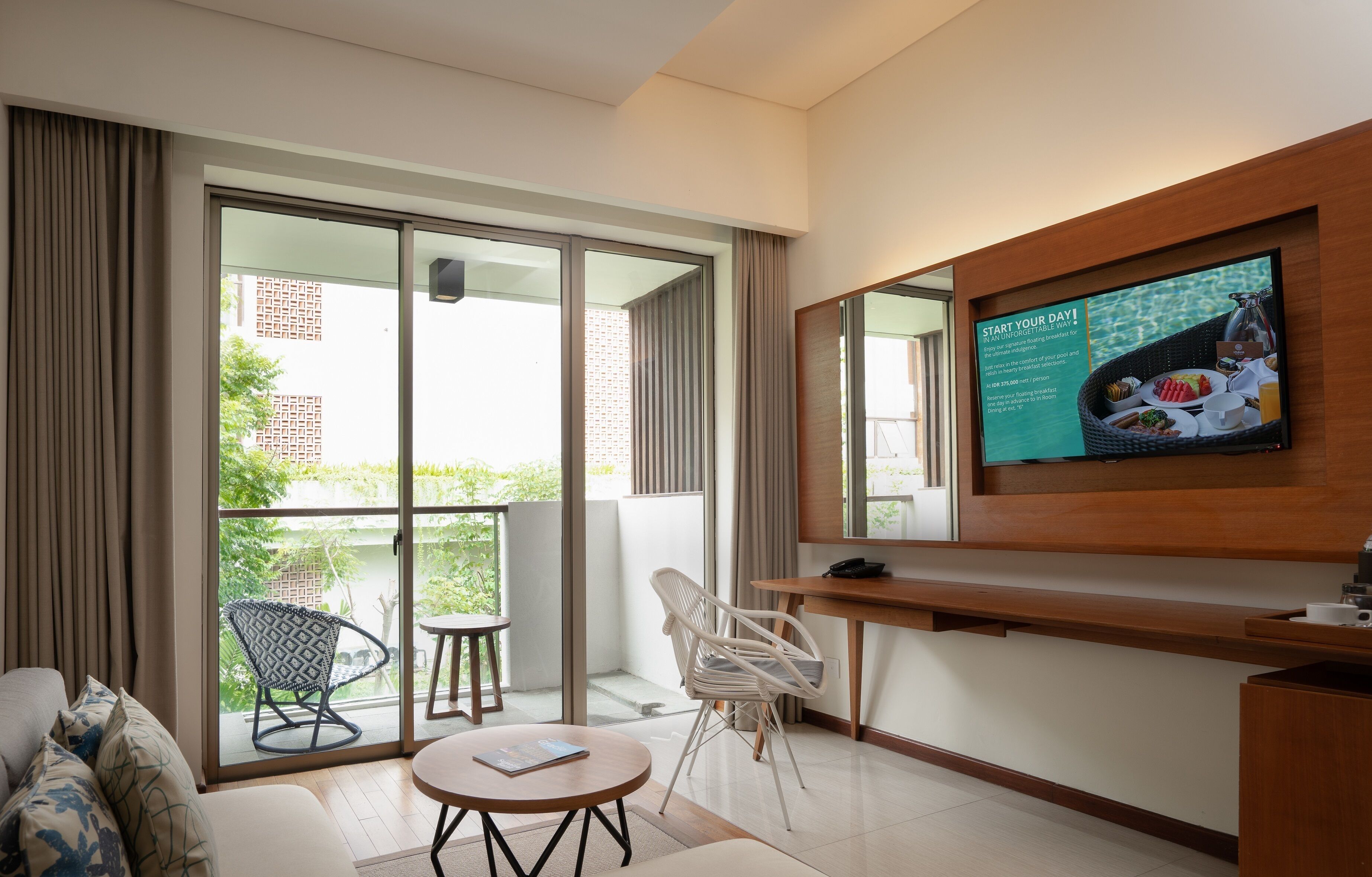 Een moderne hotelkamer met een balkon, een bank, een ronde tafel en een aan de muur bevestigde televisie.