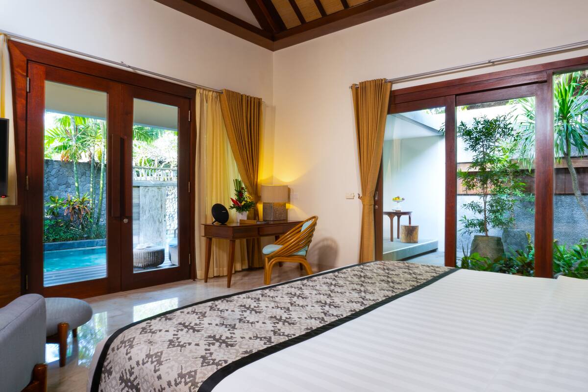 Un dormitorio con cama, escritorio, silla, televisor y vista a una piscina y jardín.