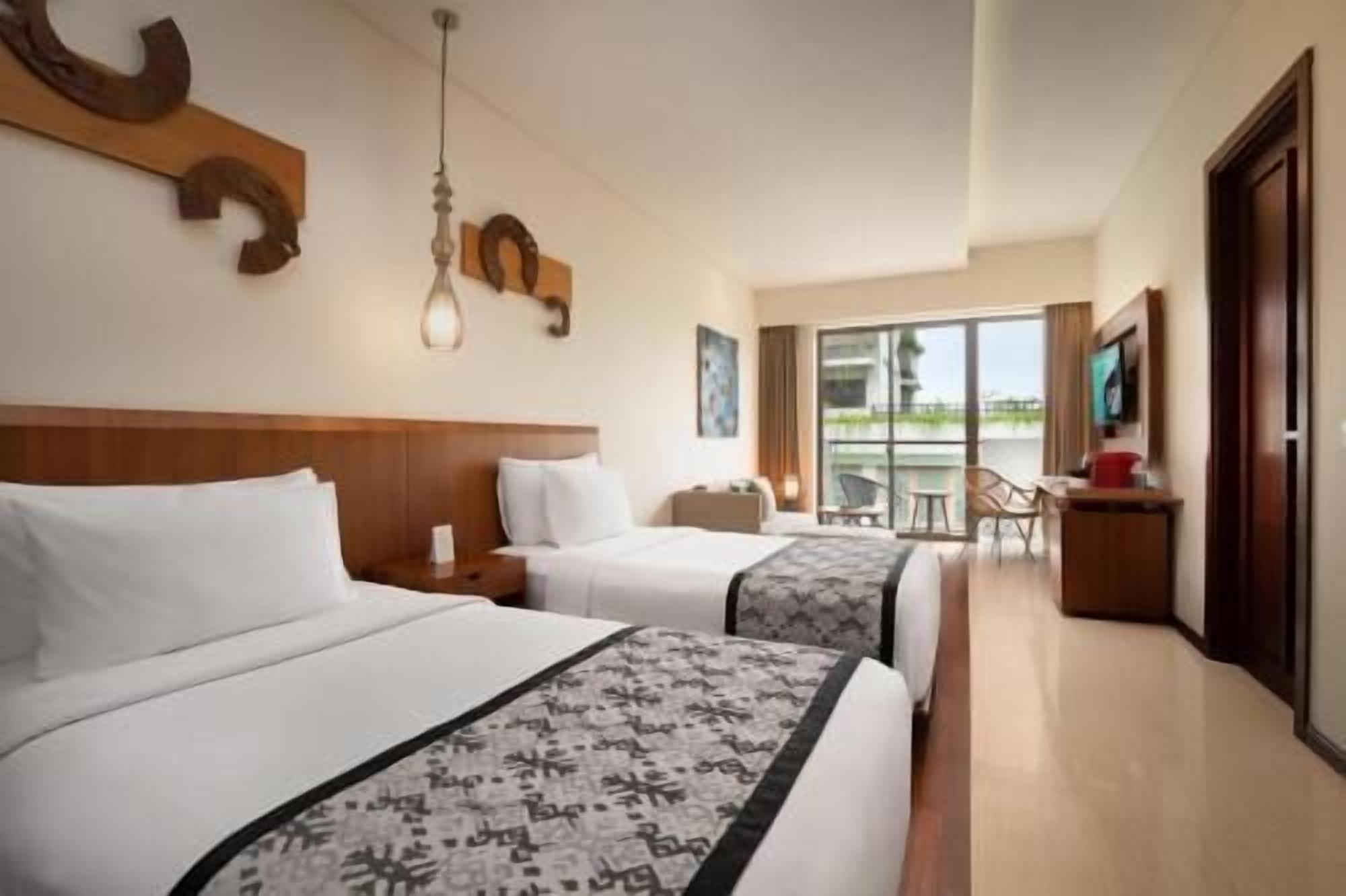 A hotel room with two beds, a desk, a chair, and a balcony with a view.