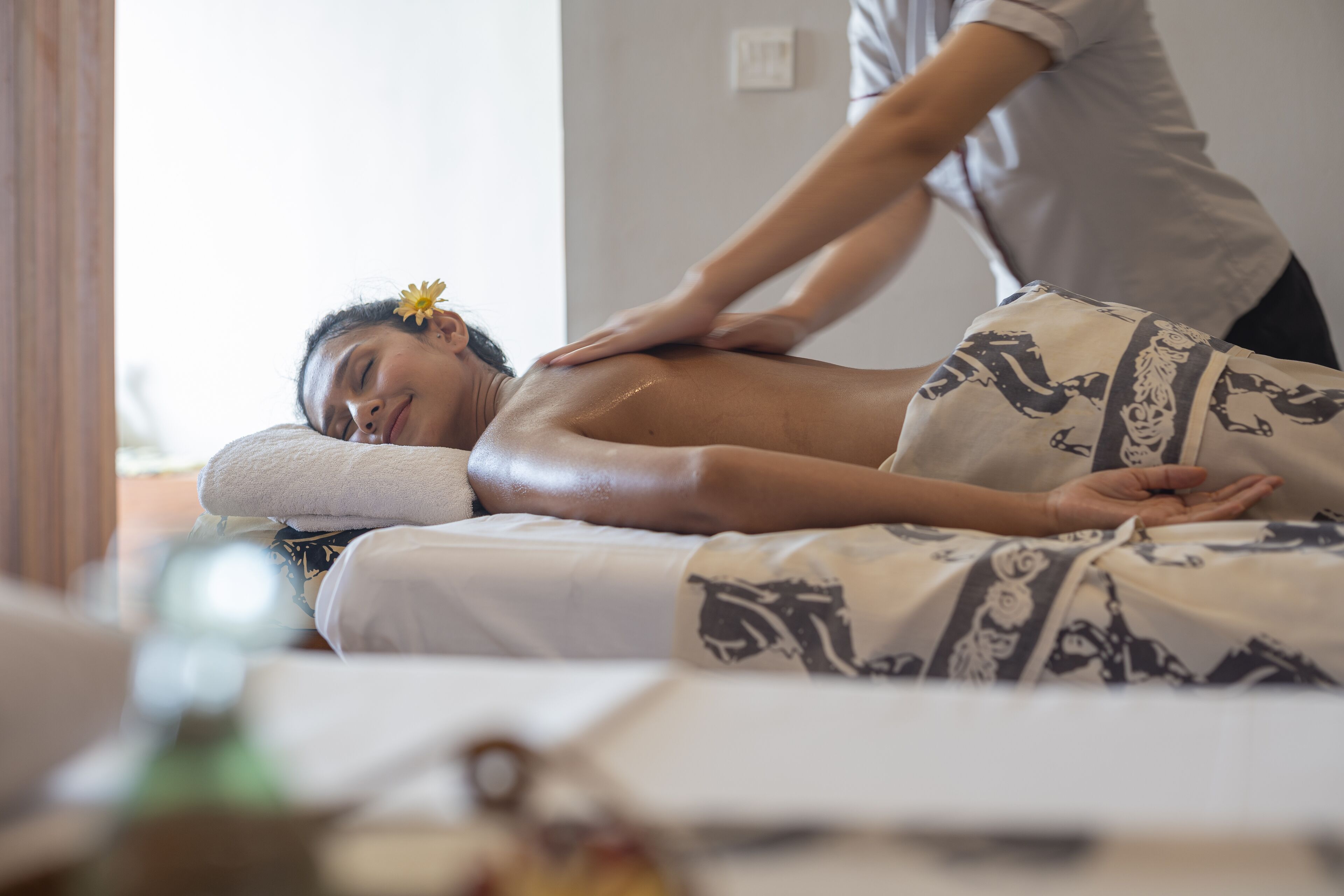 A person receiving a massage in a room with a bed covered in patterned linens.
